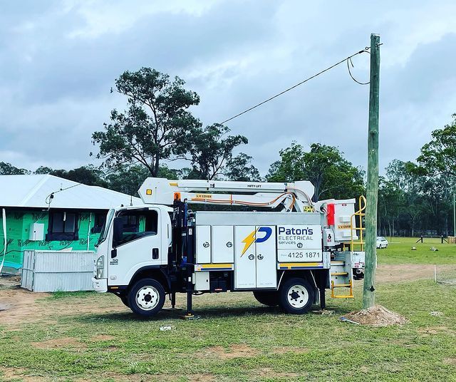 A White Truck Is Parked in A Grassy Field Next to A Pole — Paton's Electrical Services in K'Gari, QLD
