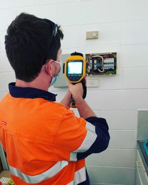 A Man In An Orange Shirt Is Holding A Yellow Device — Paton's Electrical Services in Hervey Bay, QLD