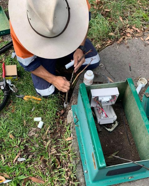 A Man Wearing a Hat Is Working on A Green Box — Paton's Electrical Services in Maryborough, QLD