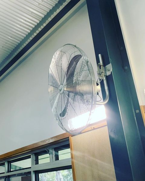 A Fan Is Mounted to A Wall Next to A Window — Paton's Electrical Services in Pialba, QLD