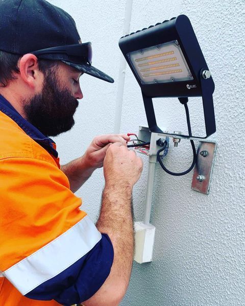 A Man Is Working on A Light on A Wall — Paton's Electrical Services in Maryborough, QLD