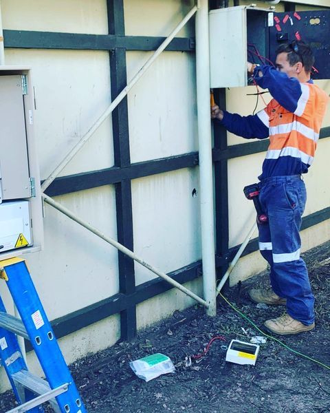 A Man Standing on A Ladder Working on An Electrical Box — Paton's Electrical Services in Maryborough, QLD