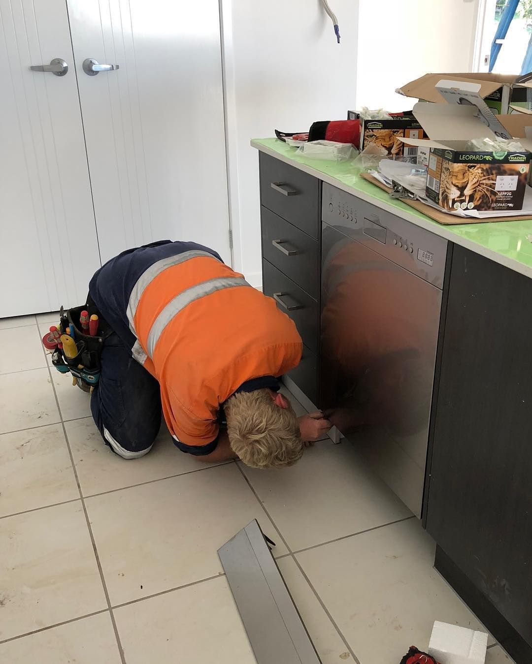 A Man Is Kneeling Down in A Kitchen Working on A Sink — Paton's Electrical Services in Torquay, QLD