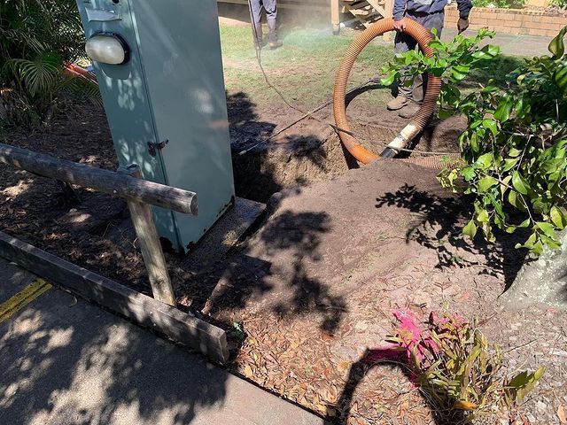 A Man Is Using a Hose to Dig a Hole in The Ground — Paton's Electrical Services in Craignish, QLD