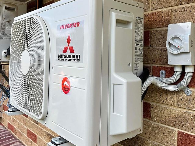 A Mitsubishi Air Conditioner Is Mounted on A Brick Wall — Paton's Electrical Services in Kawungan, QLD