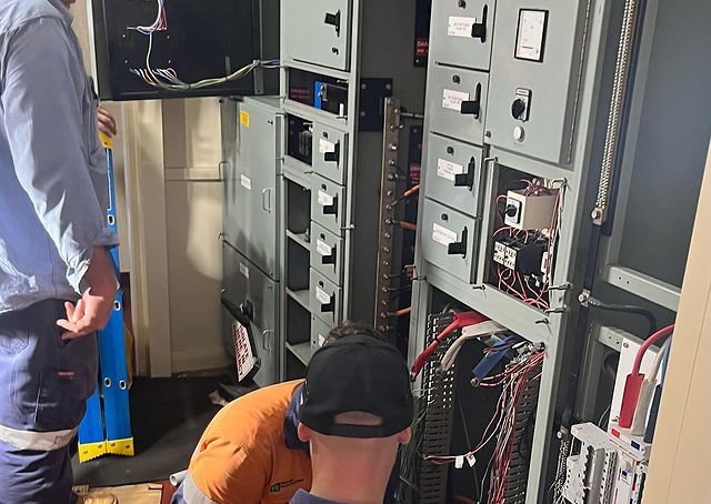 Two Men Are Working on A Electrical Panel in A Room — Paton's Electrical Services in Maryborough, QLD