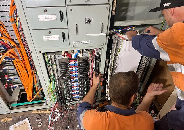 A Man Standing on A Ladder Working on An Electrical Box — Paton's Electrical Services in Craignish, QLD