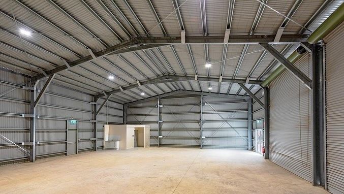 A Large Empty Warehouse with A Metal Roof and A Wooden Floor — Paton's Electrical Services in Craignish, QLD