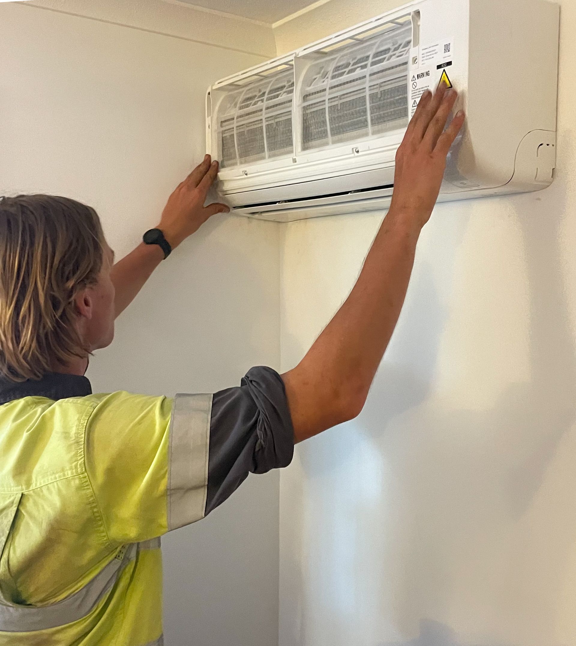 A Man Is Installing a Panasonic Air Conditioner on A Brick Wall — Paton's Electrical Services in Urangan, QLD