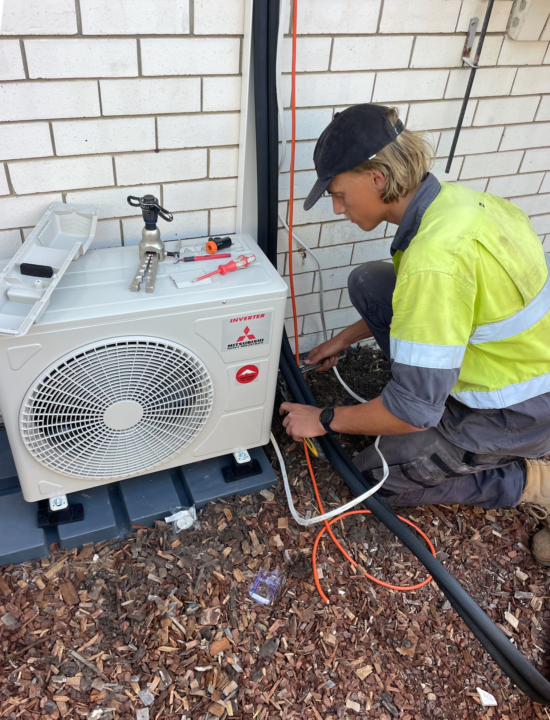 A Man Is Working on An Air Conditioner Outside of A Building — Paton's Electrical Services in Urangan, QLD