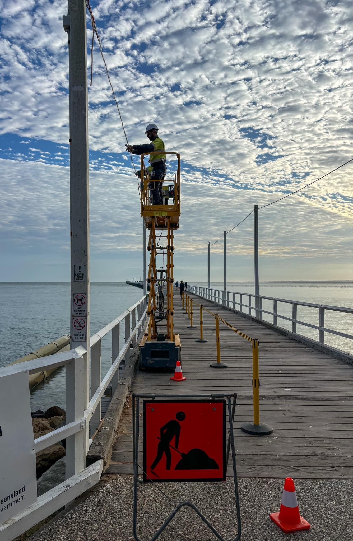 A Man Is Standing on A Lift on A Pier Overlooking the Ocean — Paton's Electrical Services in Urangan, QLD