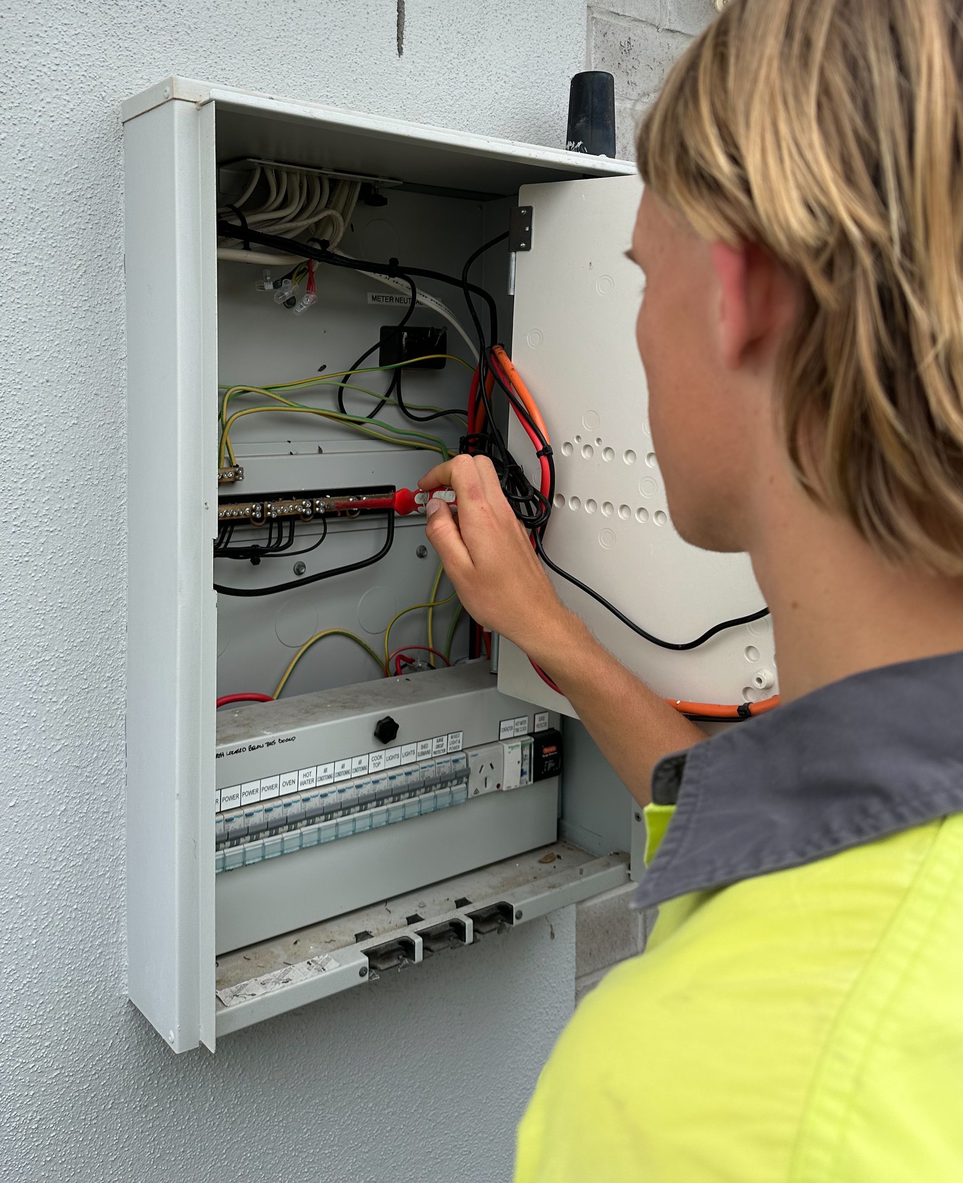 A Man in A Yellow Hi Vis Shirt Working on An Electrical Outlet — Paton's Electrical Services in Urangan, QLD