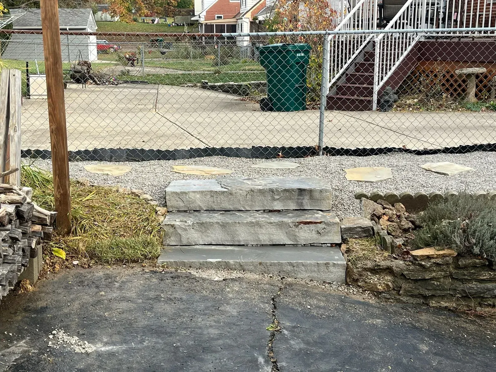 Concrete steps leading up to a chain-link fence and yard. Green trash can and brown deck visible in the background.