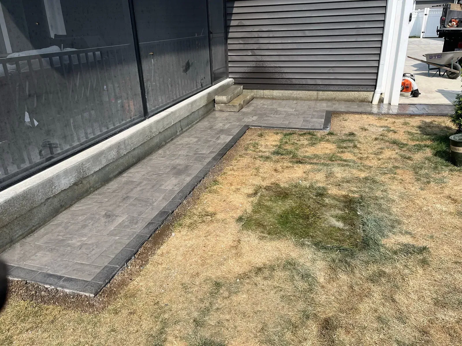 Gray stone walkway next to building with steps and dry grass.