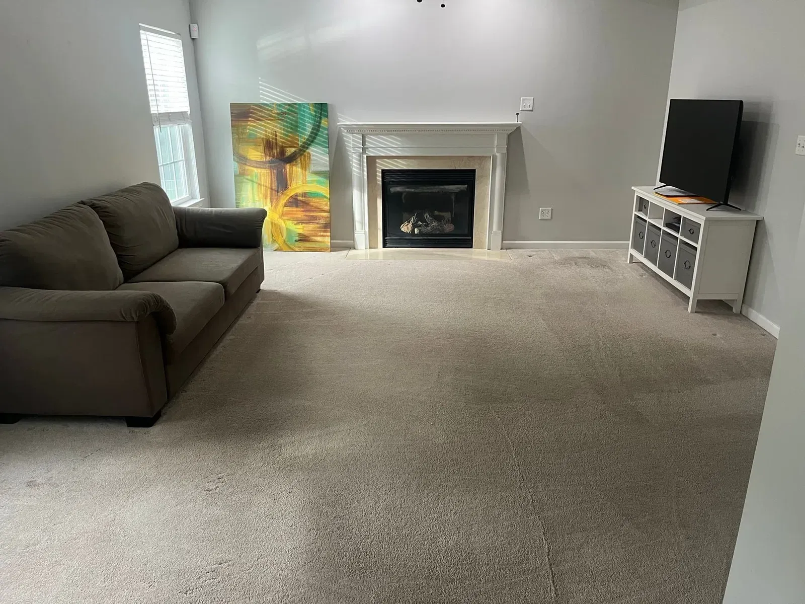 Living room with gray walls, carpet, sofa, fireplace, TV, and artwork.