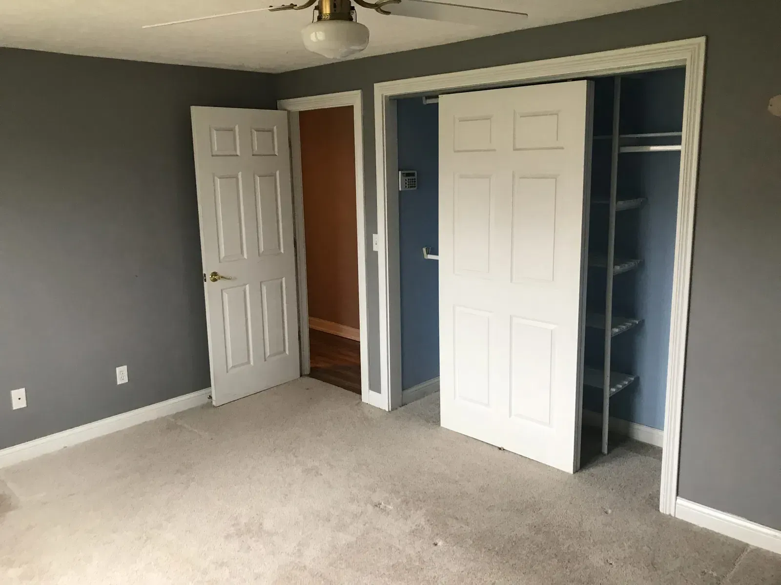 Bedroom with gray walls, carpet, white closet doors, and an open door to another room.