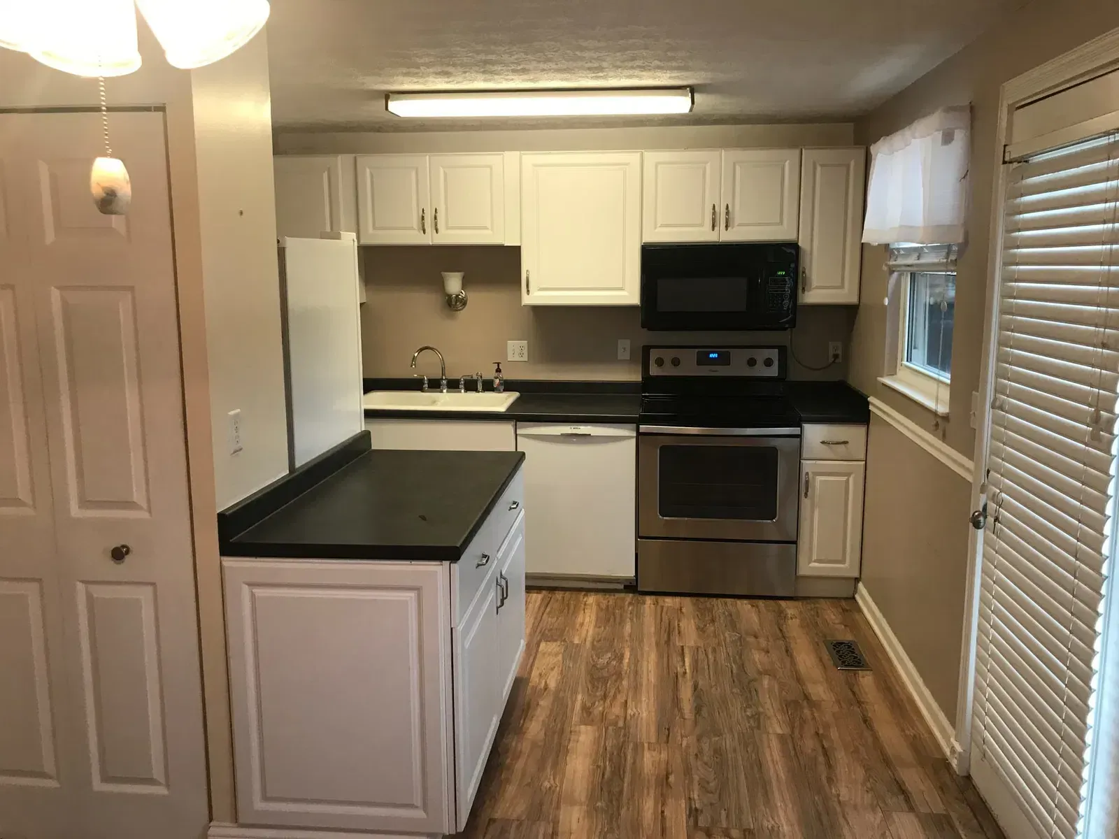 Small kitchen with white cabinets, black countertops, and stainless steel appliances; wooden floor.