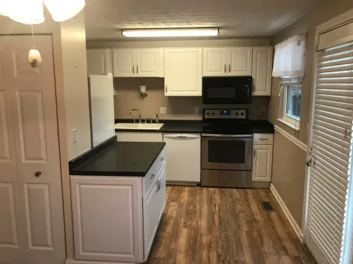 Kitchen with white cabinets, black countertops, stainless steel appliances, and wooden floor.