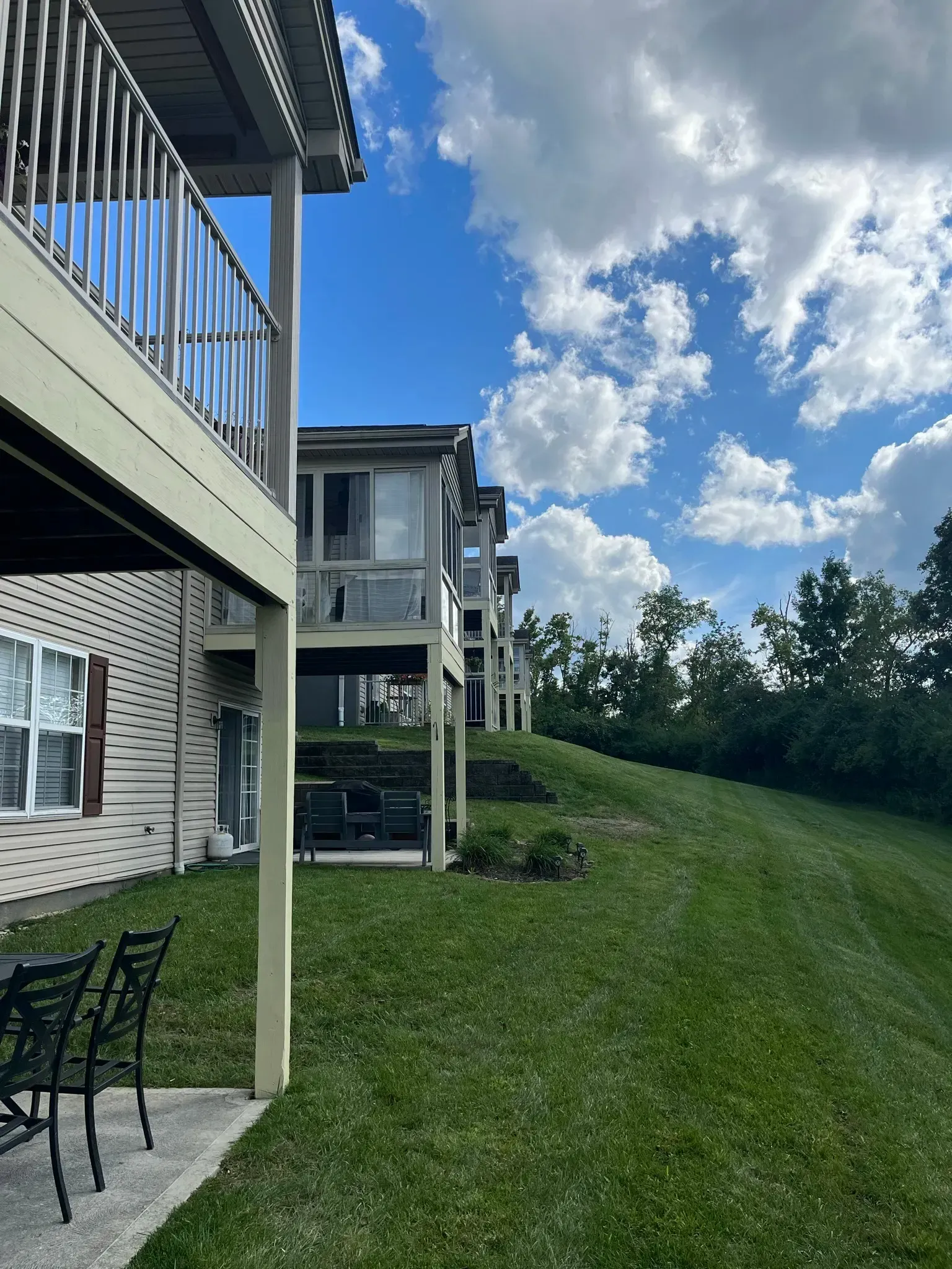 Apartment buildings with balconies on a grassy hill under a bright blue sky with fluffy white clouds.