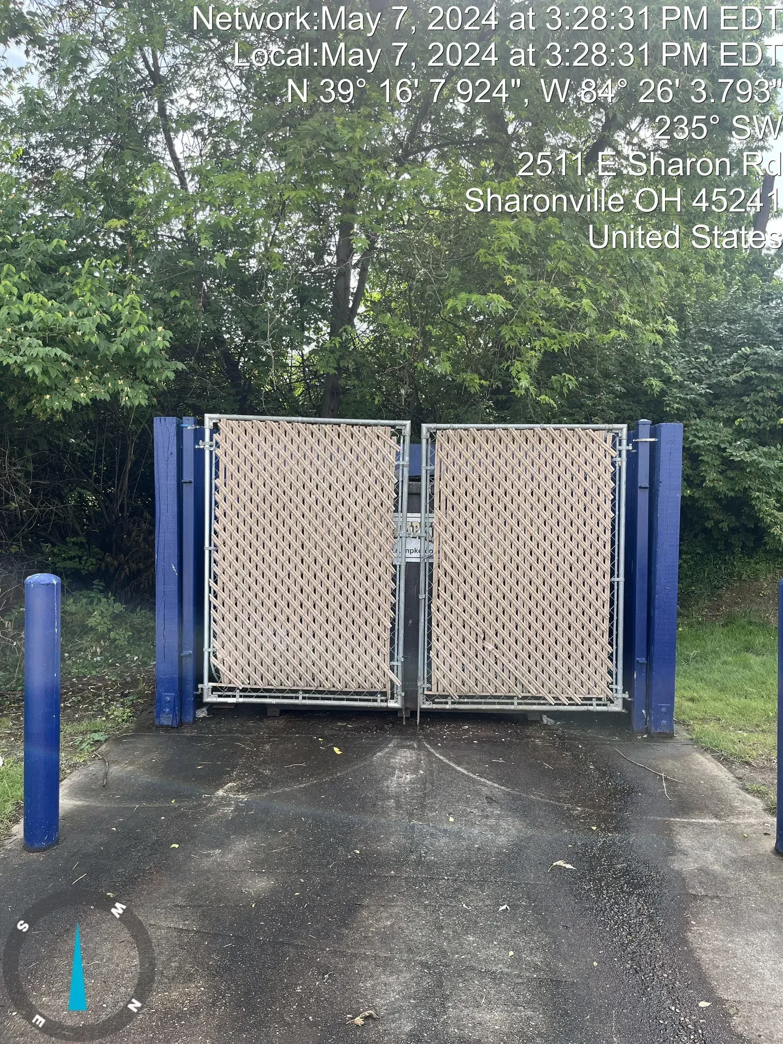 Blue gate with woven panels, on a concrete path, surrounded by trees.