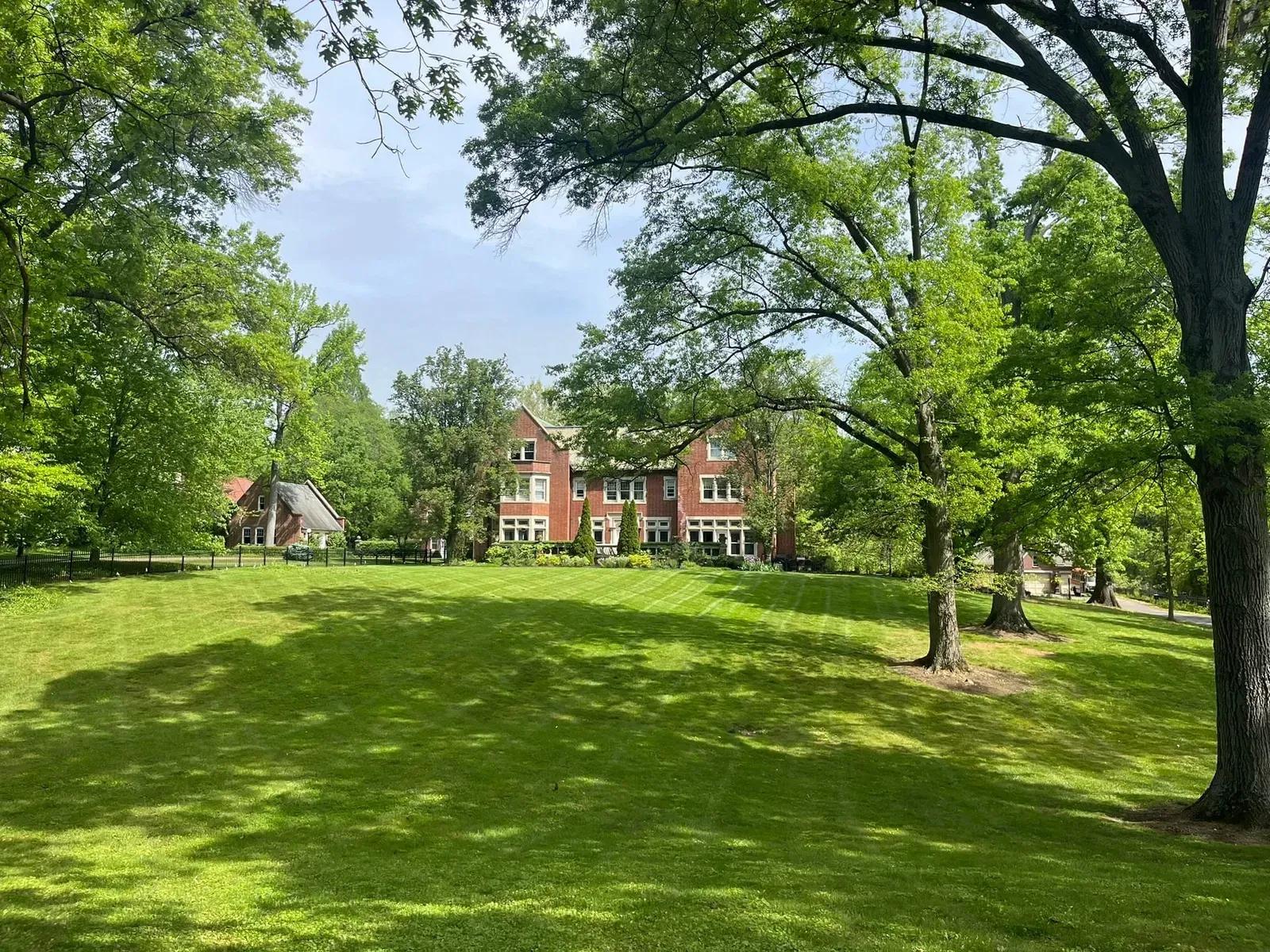 Brick house nestled among green trees on a sunny day.