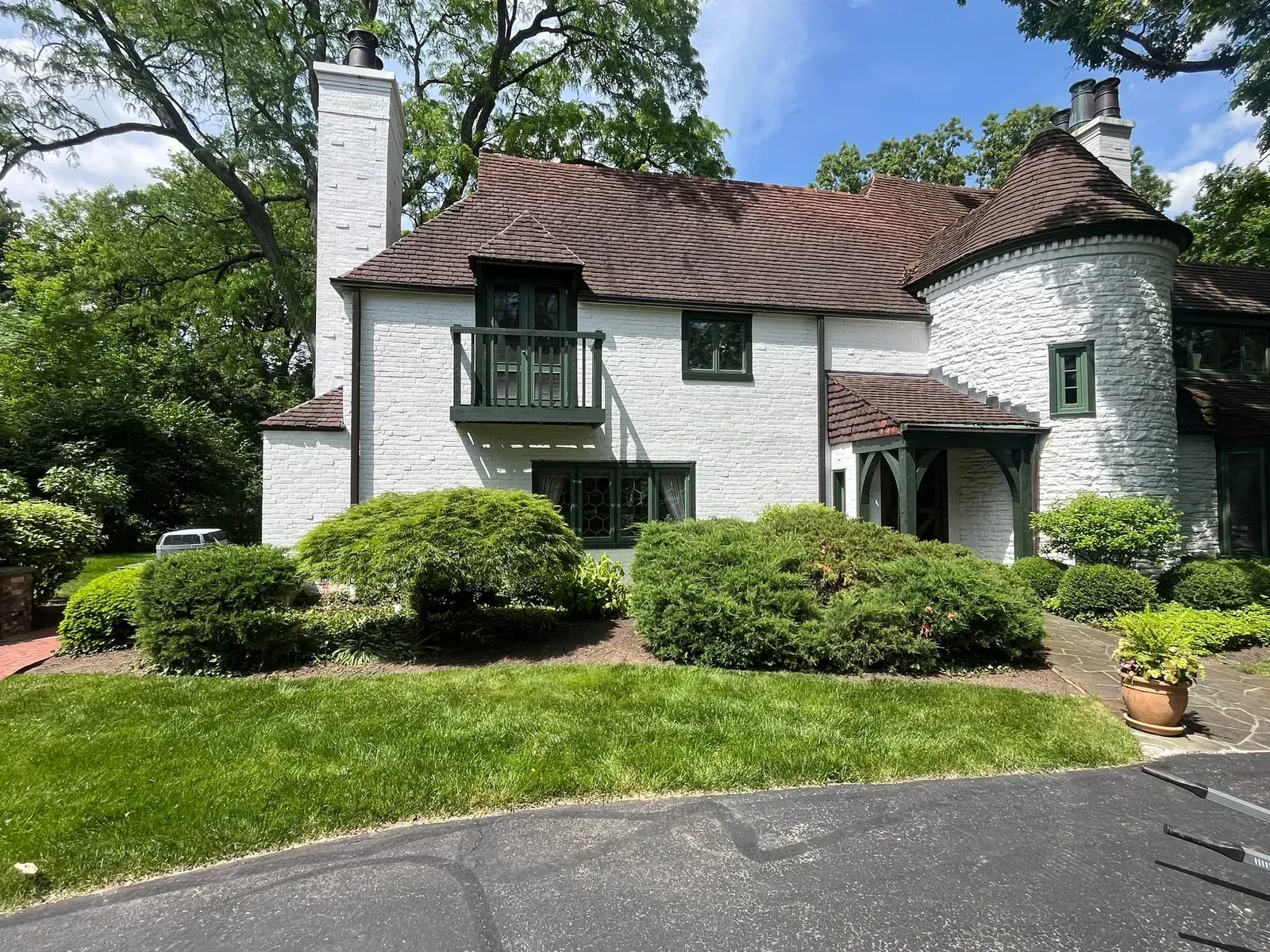 White house with dark green trim, brown roof, and lush landscaping.