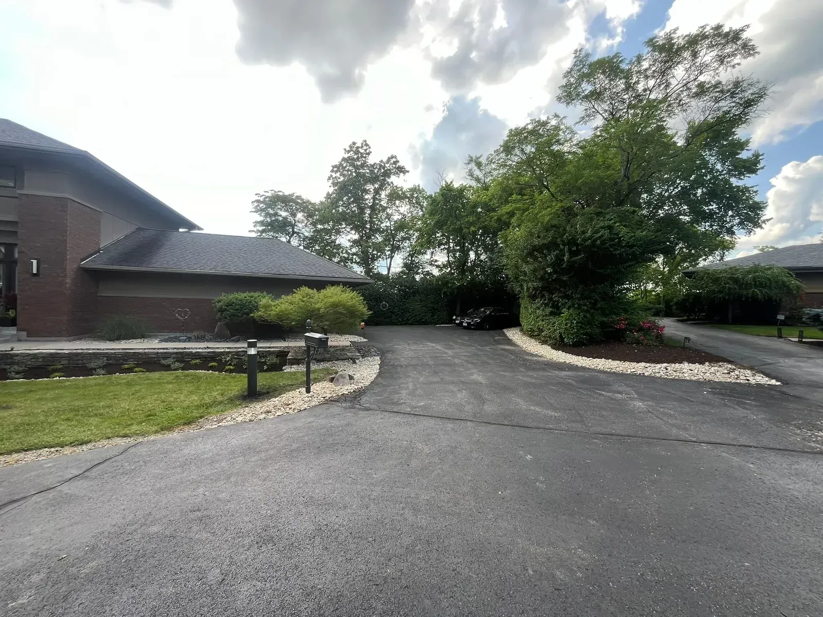 Driveway leading to a building with trees, bushes, and blue sky.