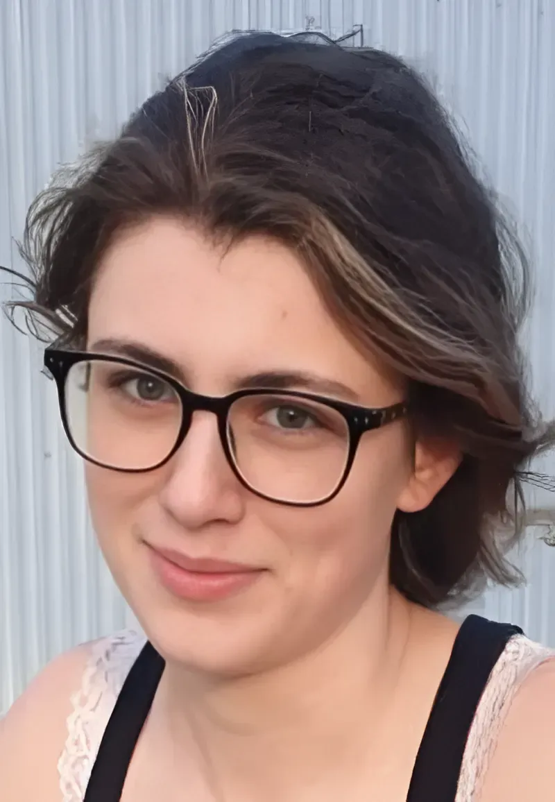 Woman with glasses, short brown hair with blonde highlights, smiling. Wearing a black tank top.