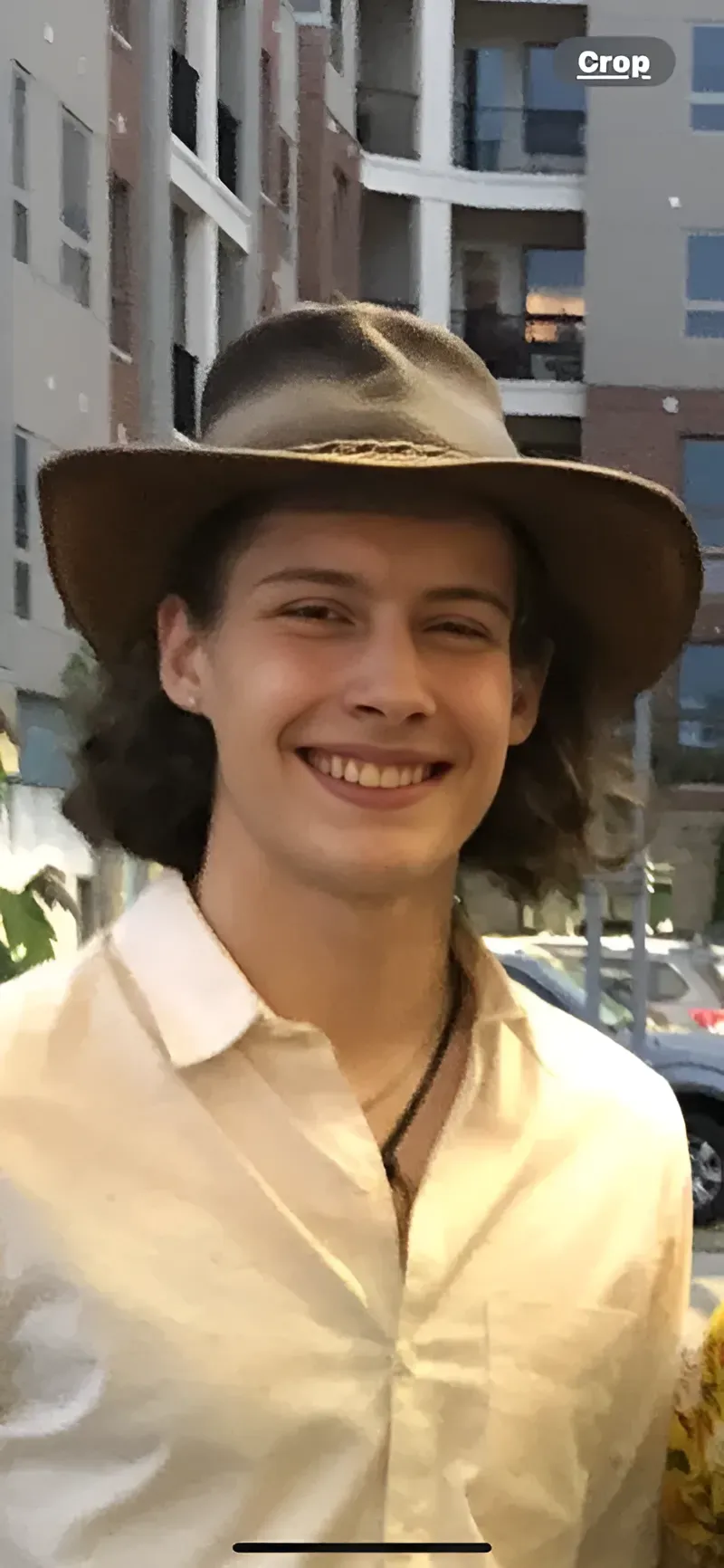 Young man in hat and white shirt smiles, outdoors.