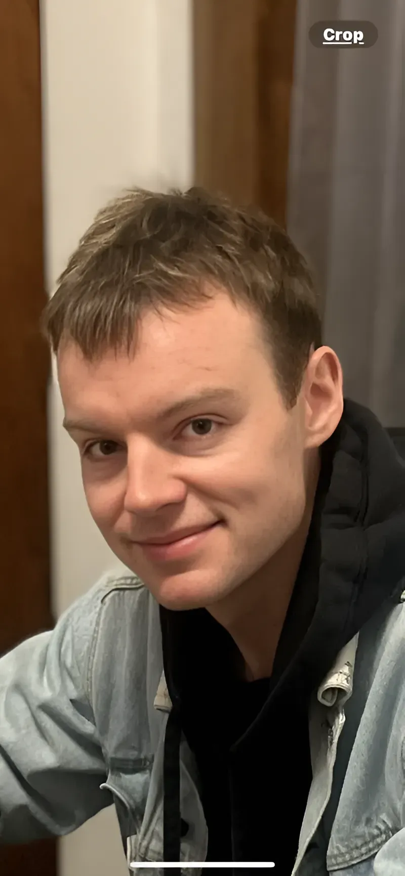 A young man with light brown hair and a slight smile, wearing a denim jacket and black hoodie.