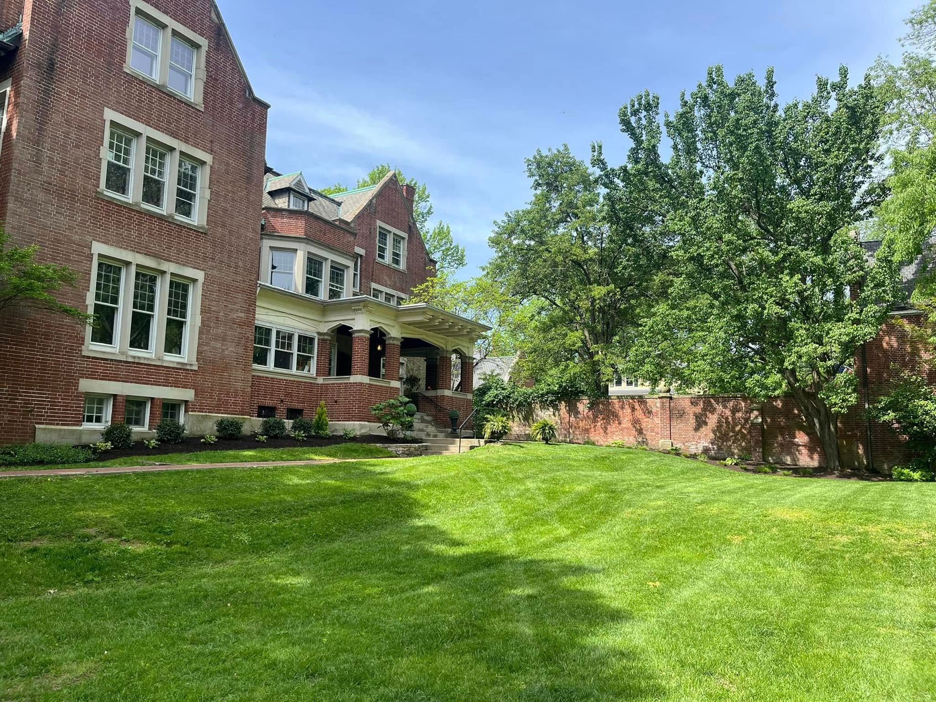 Red brick multi-story building with a green lawn, trees, and a blue sky.