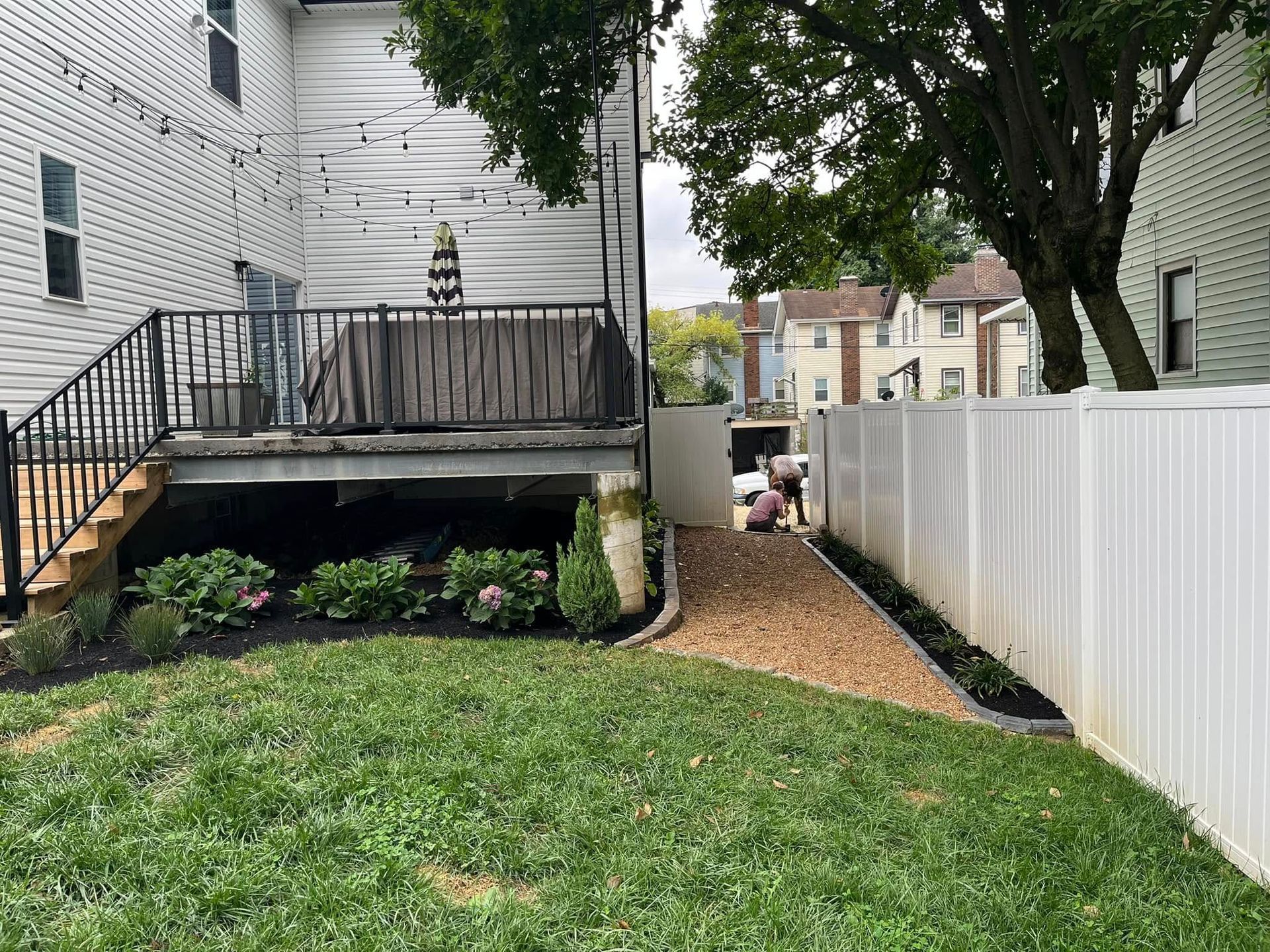 Backyard with a deck, gravel path, white fence, and green grass.