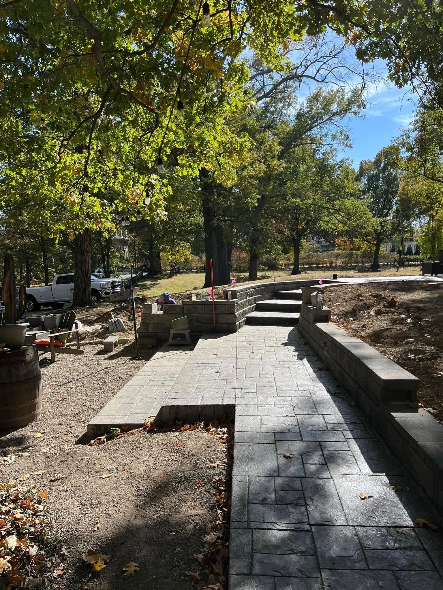 Stone pathway under construction leading up to stairs, surrounded by trees and dirt.