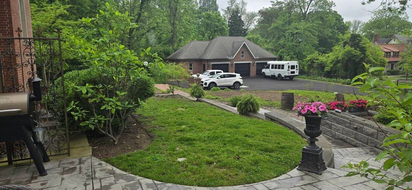 Lush green yard with a stone pathway leading to a two-car garage. White SUV and van parked.