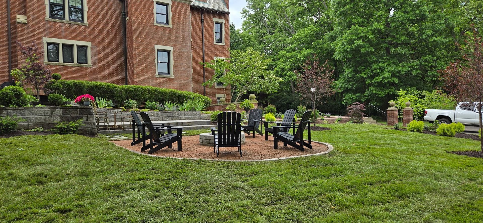 A brick building with a lawn area and fire pit seating. White pickup truck visible.
