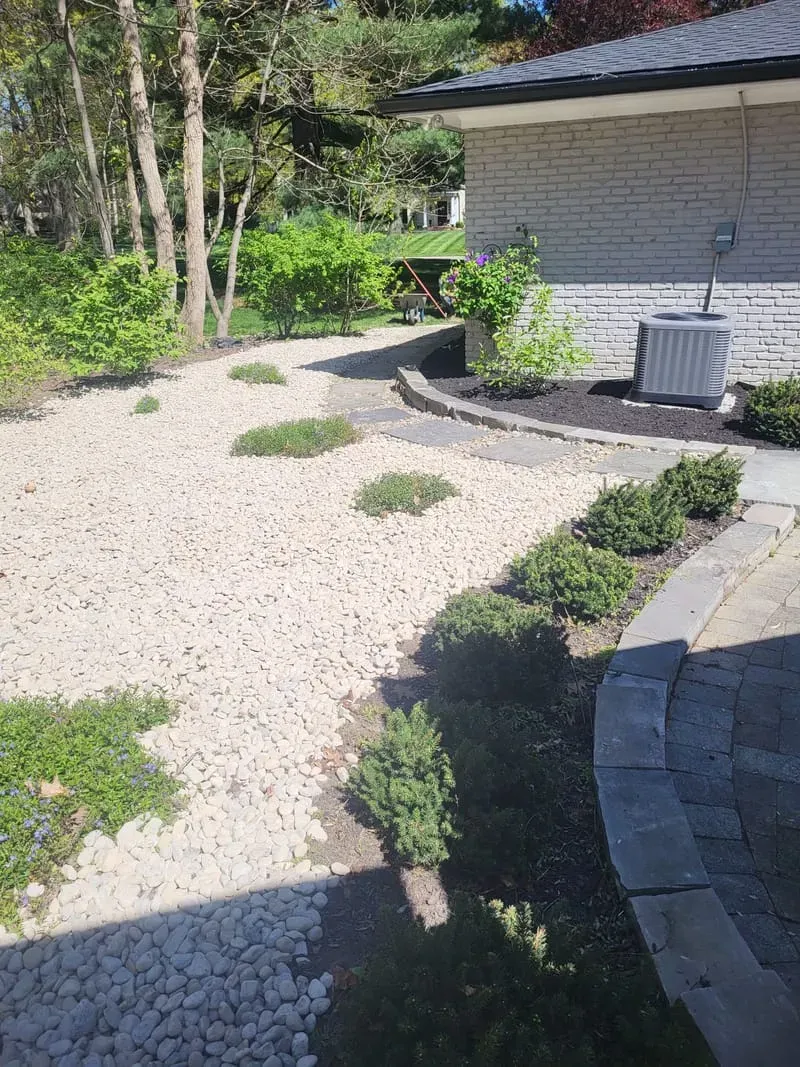 Stone-covered landscaping with small plants. A brick building and pathway border the area.