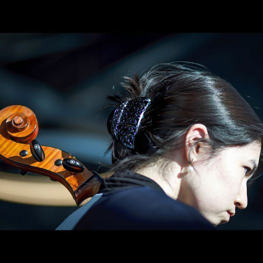 A woman is playing a cello with her hair in a bun