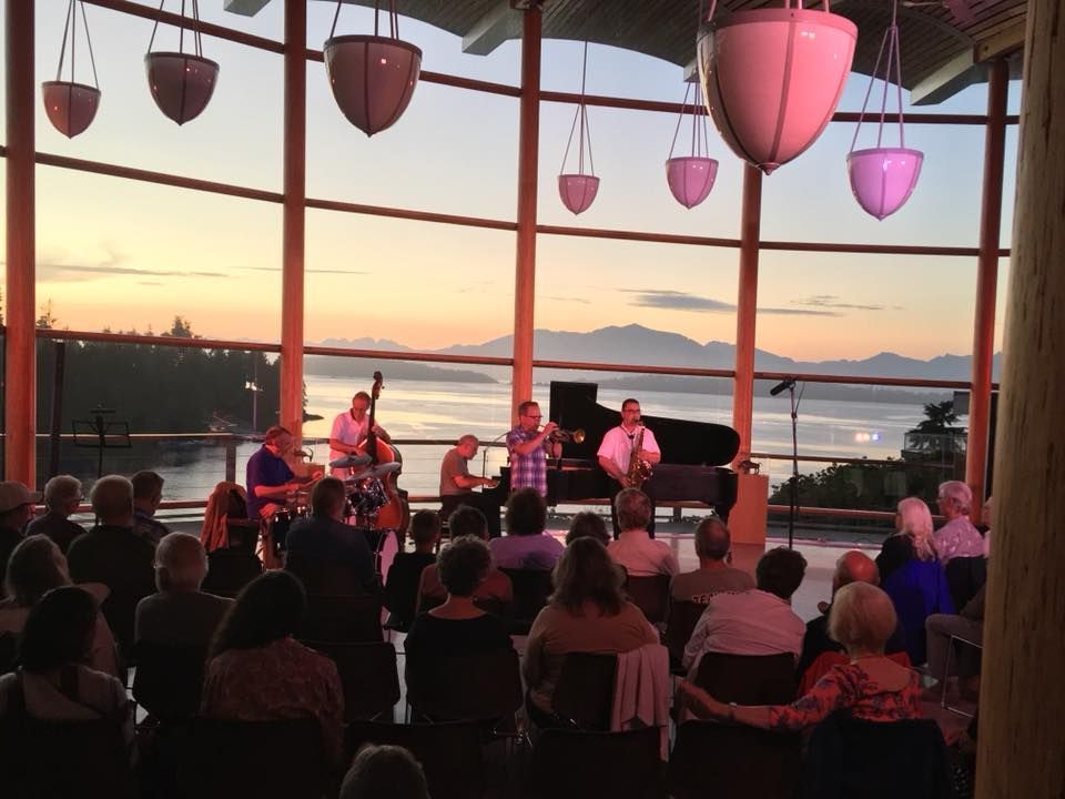 A group of people are sitting in front of a large window watching a band perform