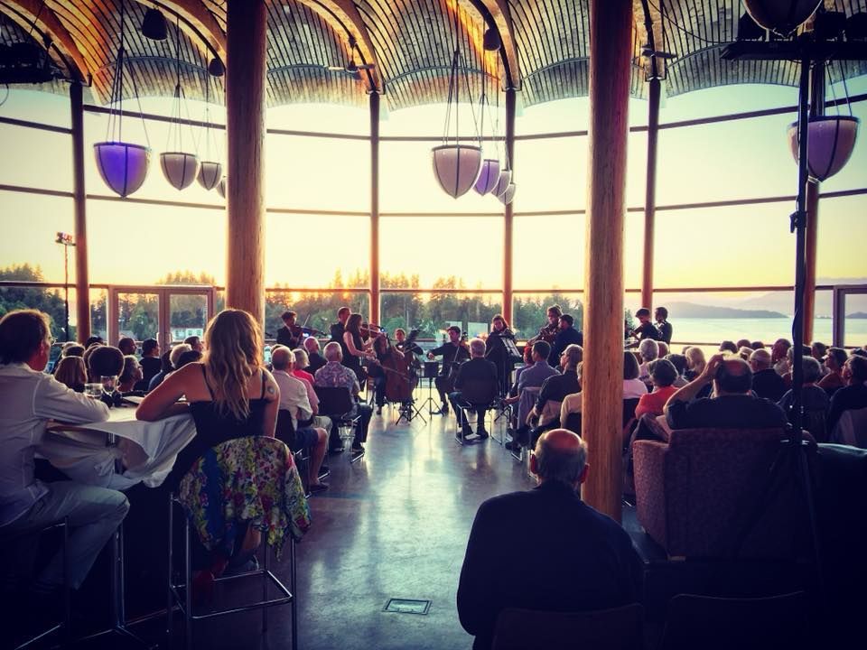 A group of people are sitting in a large room watching a concert.