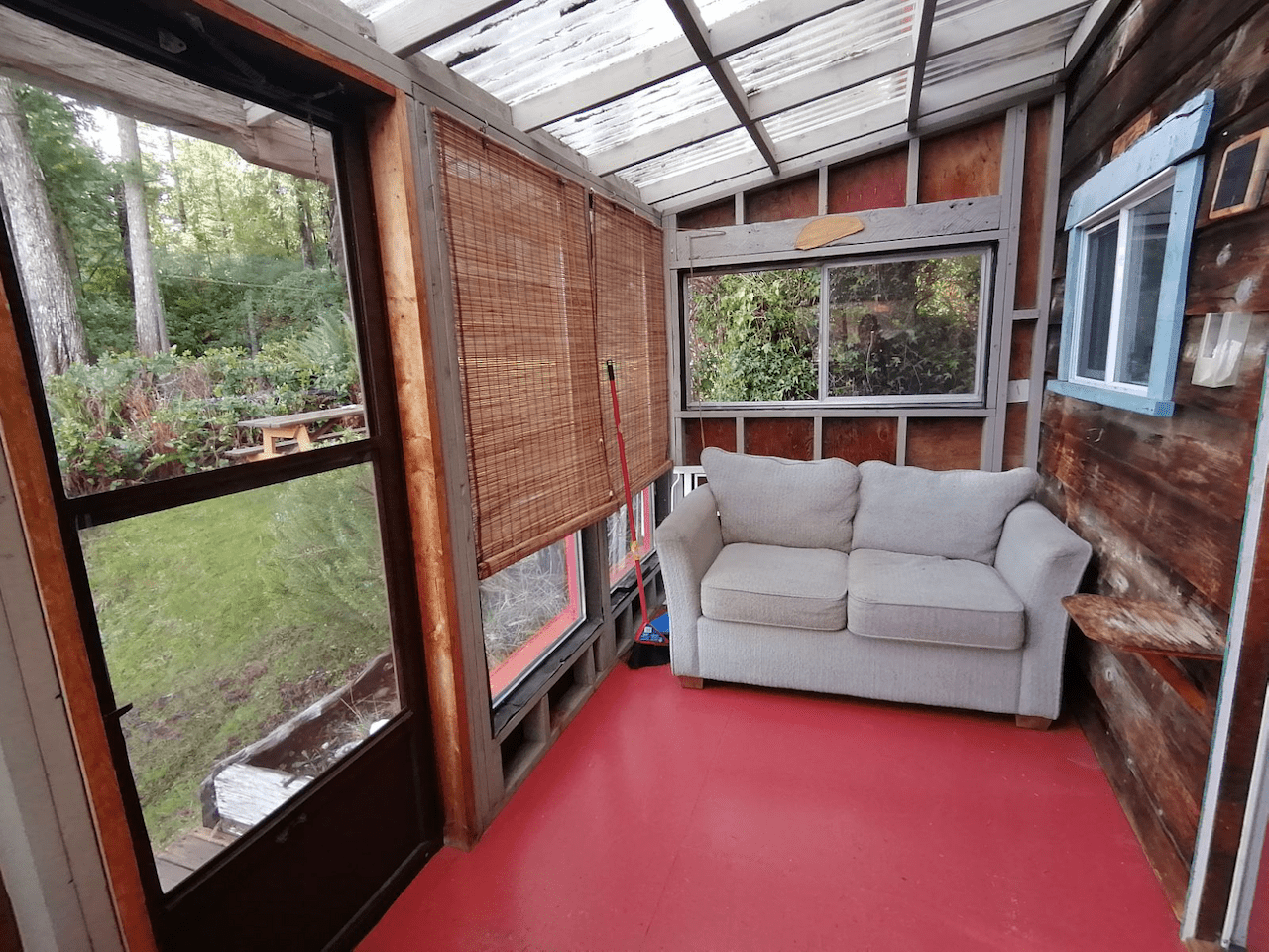 There is a couch in the sunroom with a red floor.