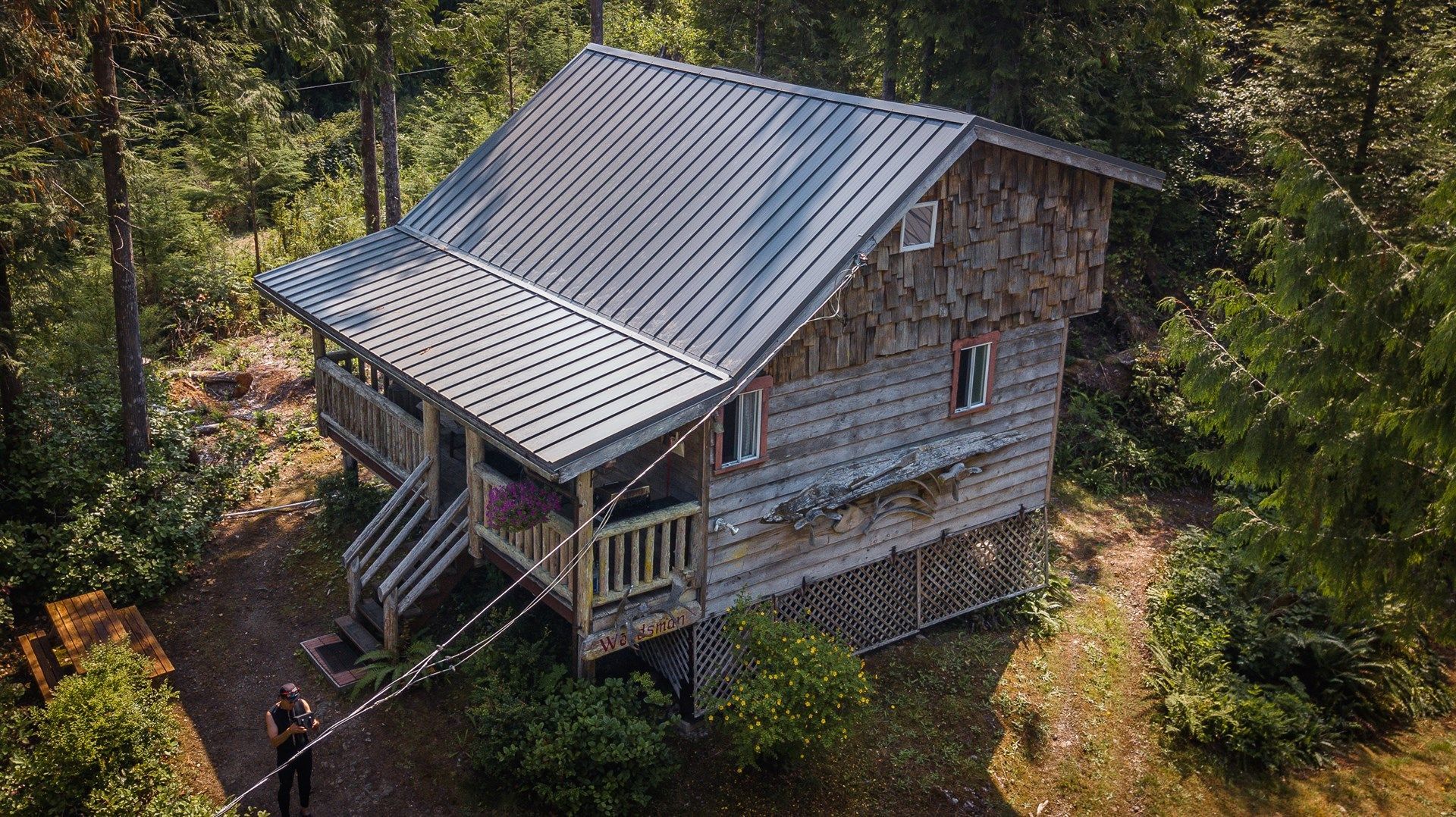 An aerial view of a small wooden cabin in the middle of a forest.
