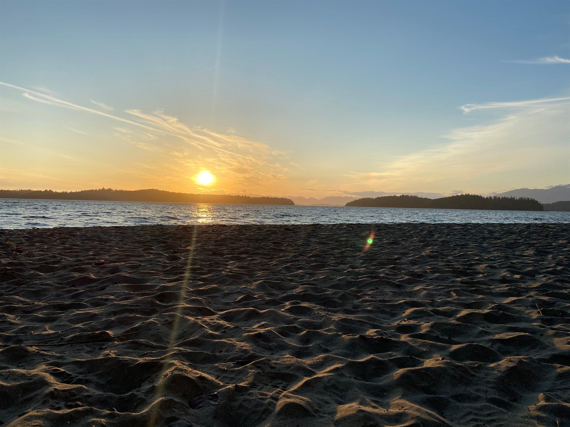 The sun is setting over a body of water on a beach.