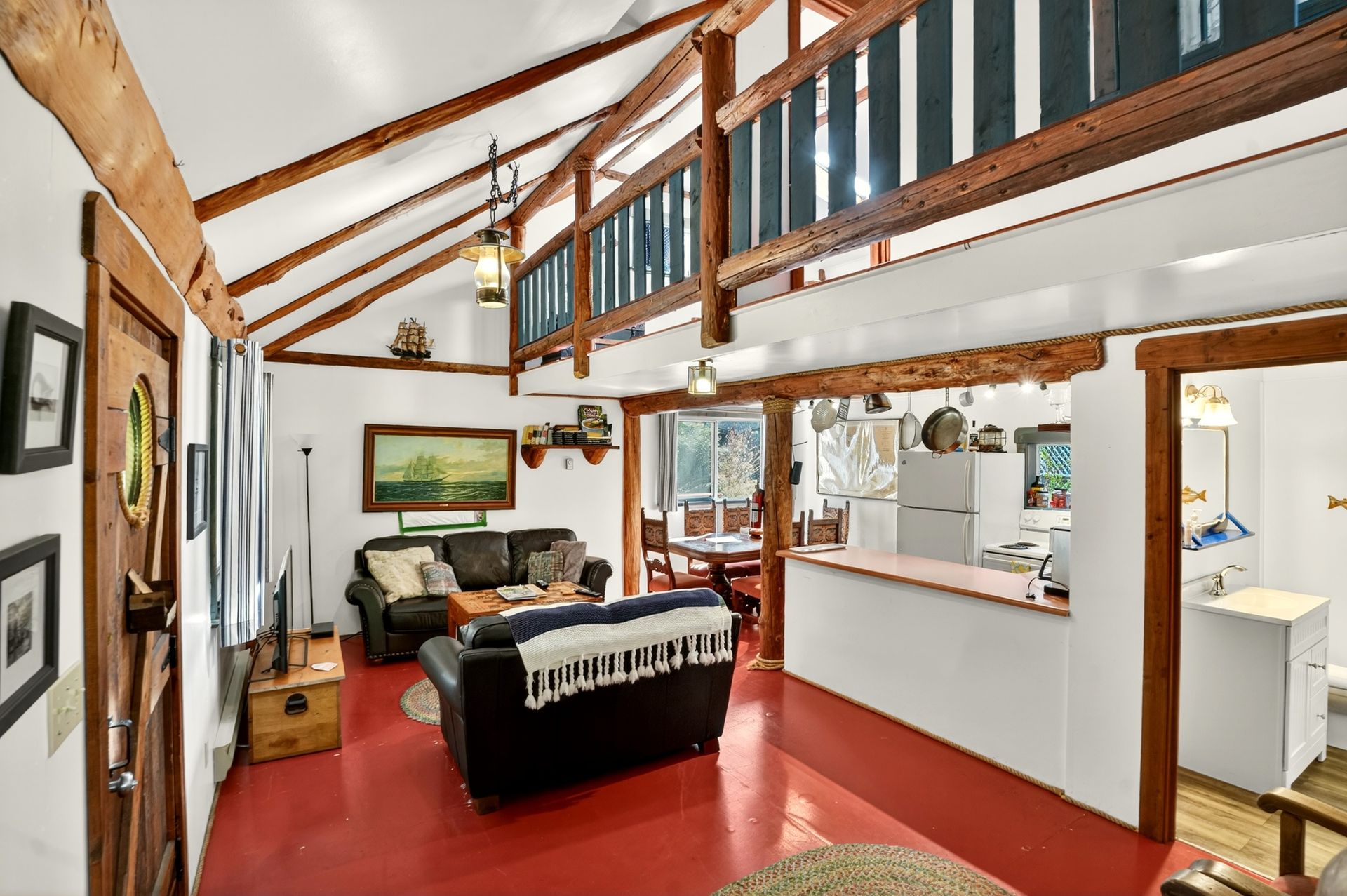 A two story log cabin in the forest by the ocean surrounded by trees.