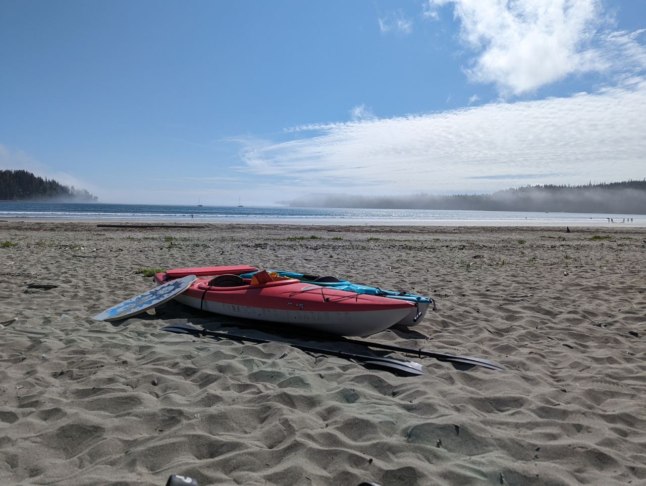A pink and white kayak is sitting on a sandy beach.