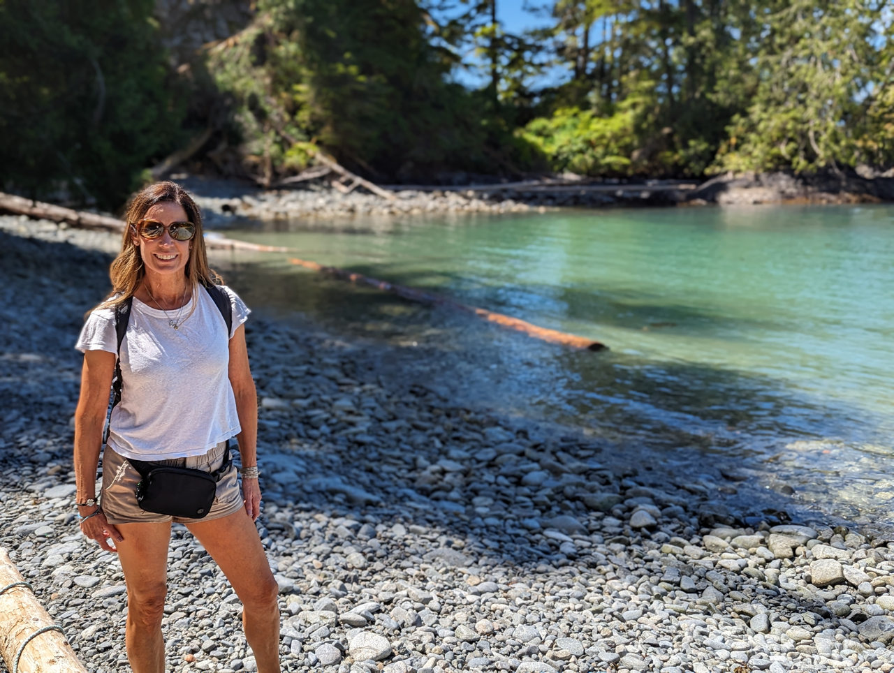 A woman is standing on a rocky beach next to a body of water.