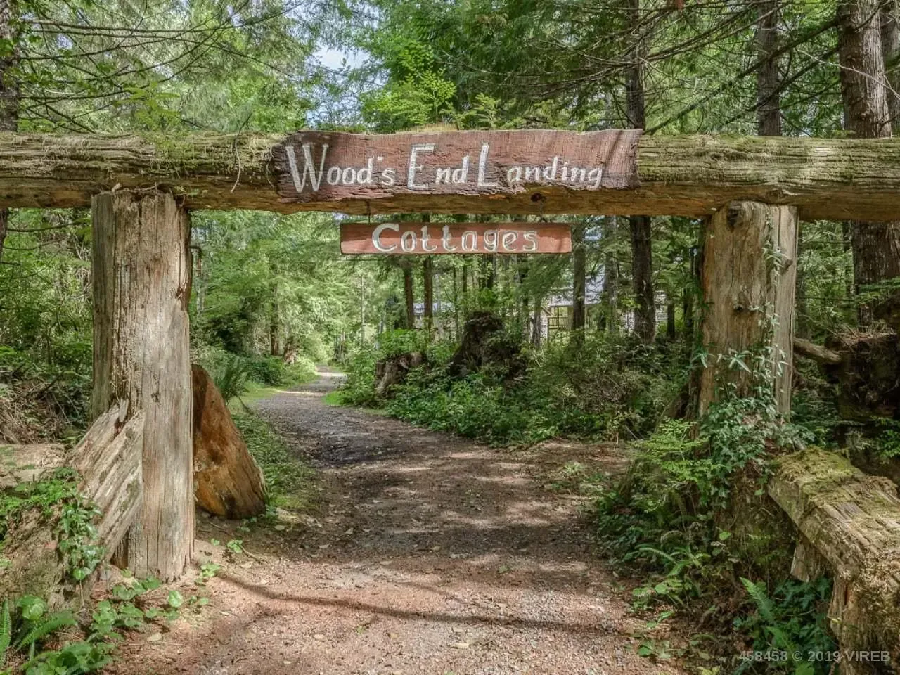 A wooden sign over a dirt path in the woods.