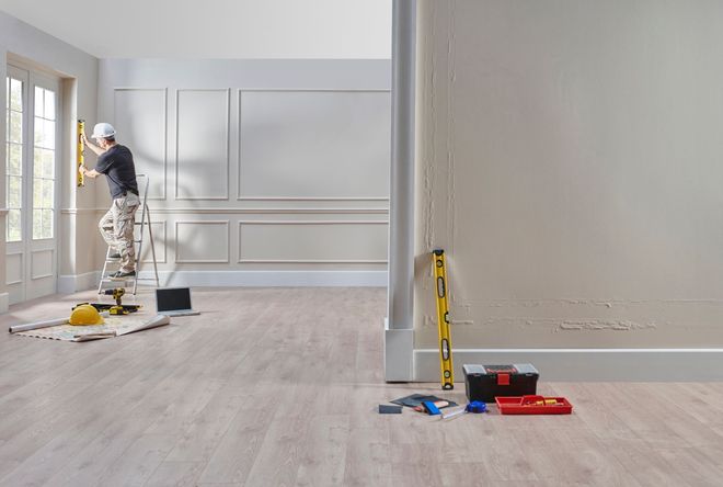 Person on ladder levels a wall in a room during renovation, with tools nearby.