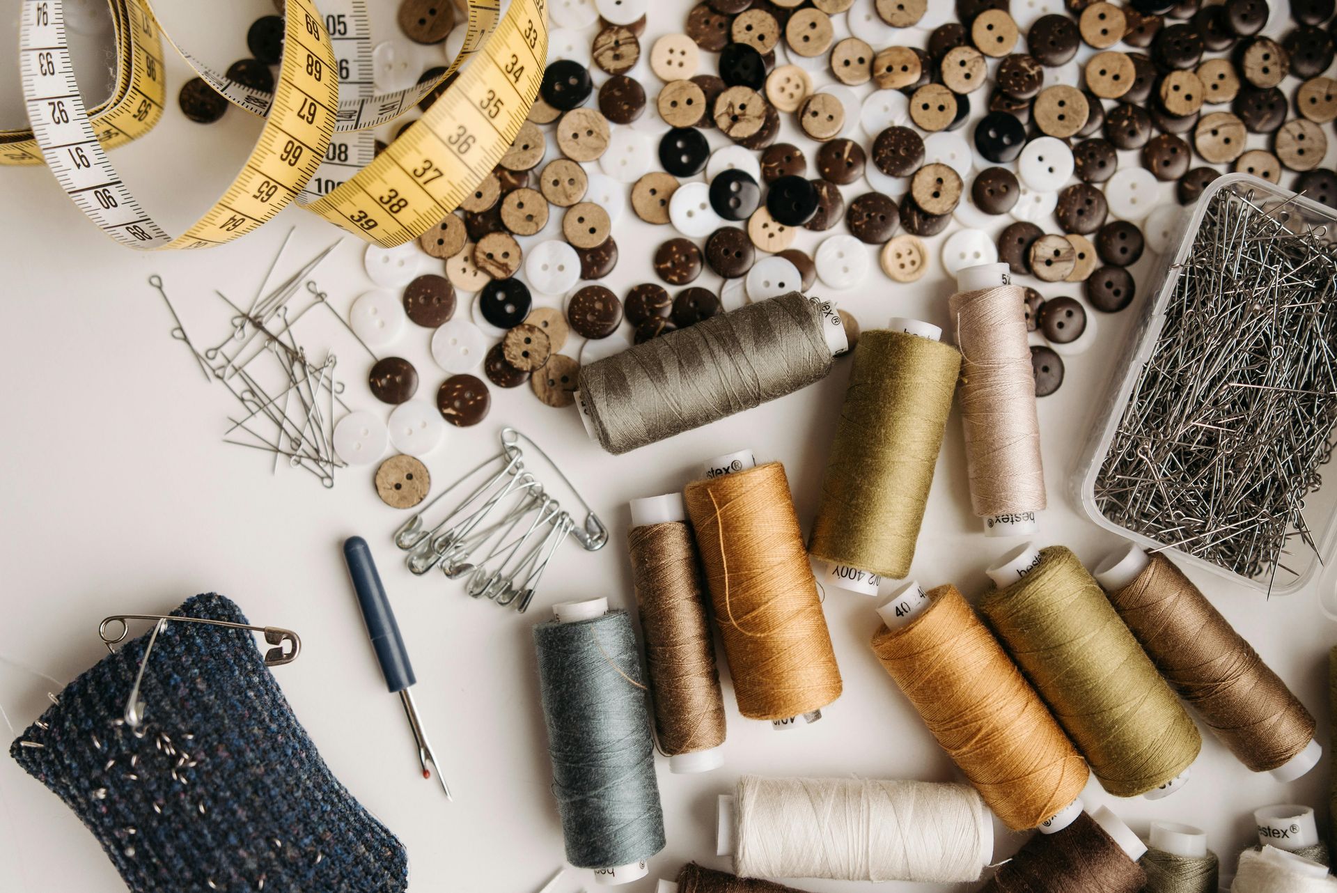 A table topped with spools of thread , buttons , pins , and a measuring tape.