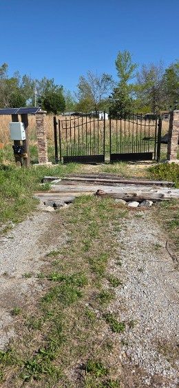 Gravel path leading to a black metal gate in a rural yard under a clear blue sky.