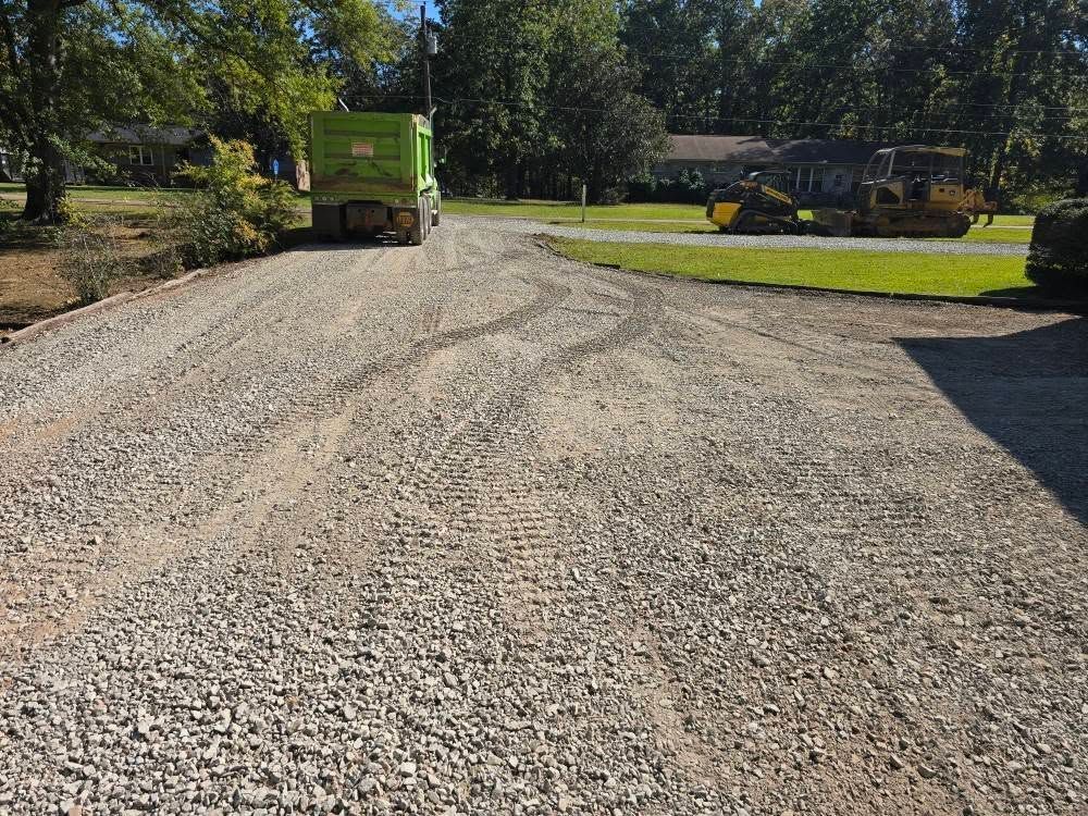 A gravel driveway with a green truck and a yellow bulldozer.